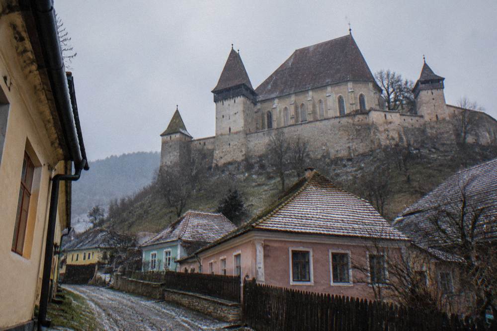 A fortified church with tall defensive walls beside a village lane in rural Transylvania