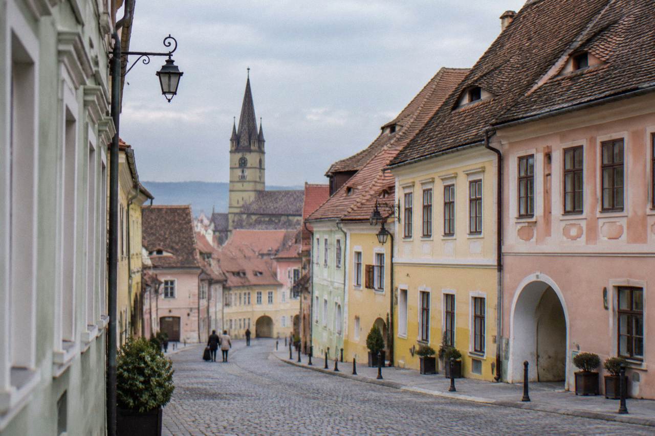 Pastel-coloured houses along a Sibiu old town street under a partly cloudy sky