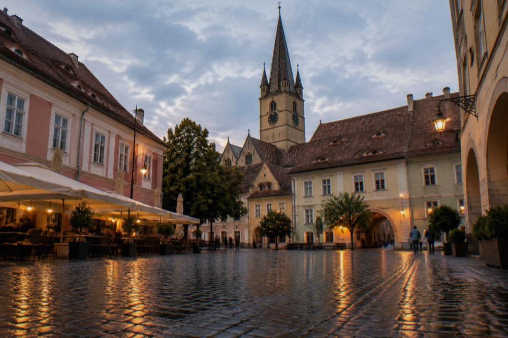 Rain-darkened cobblestones of a Sibiu square reflecting café lights in the evening