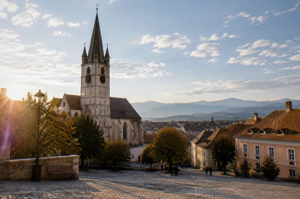 A viewpoint over Sibiu's rooftops with mountains visible on the horizon under scattered clouds
