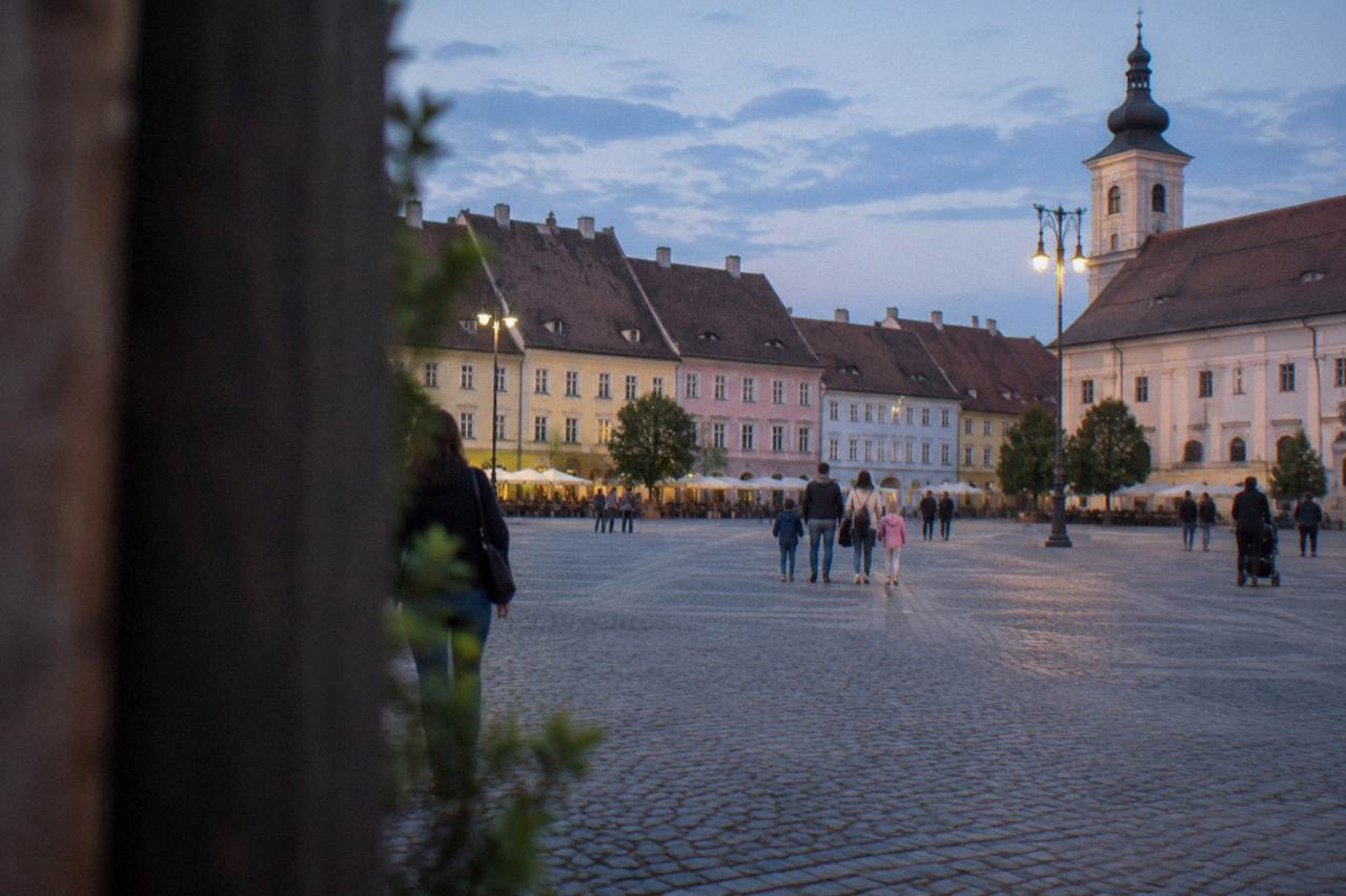 Families walking across a large cobbled square ringed by colourful historic buildings