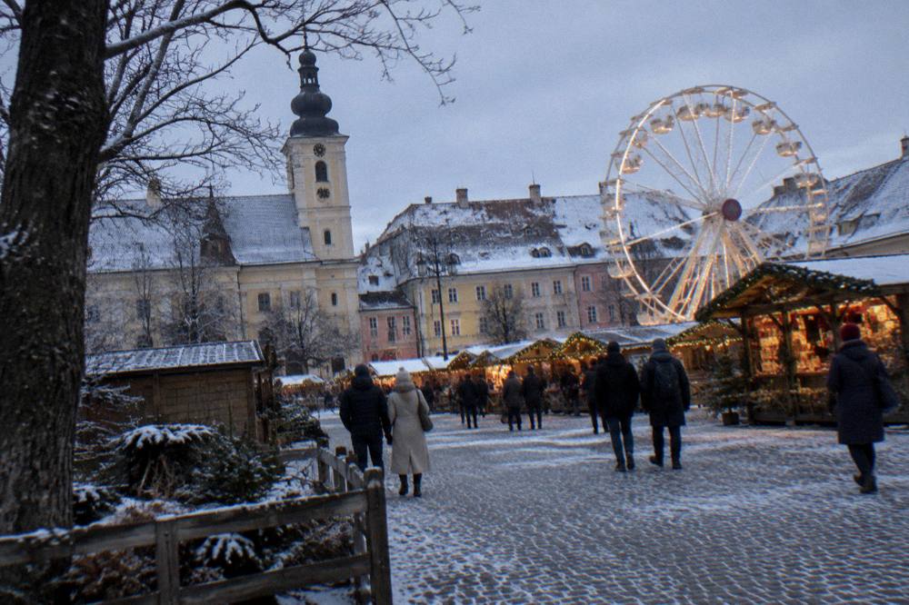 A Christmas market with wooden stalls and a ferris wheel in a snowy old square