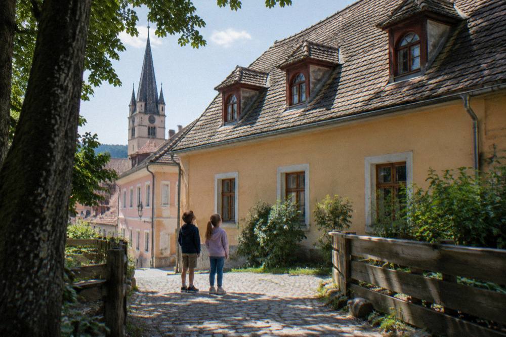 Two children looking up at the steep dormer windows on an old tiled roof