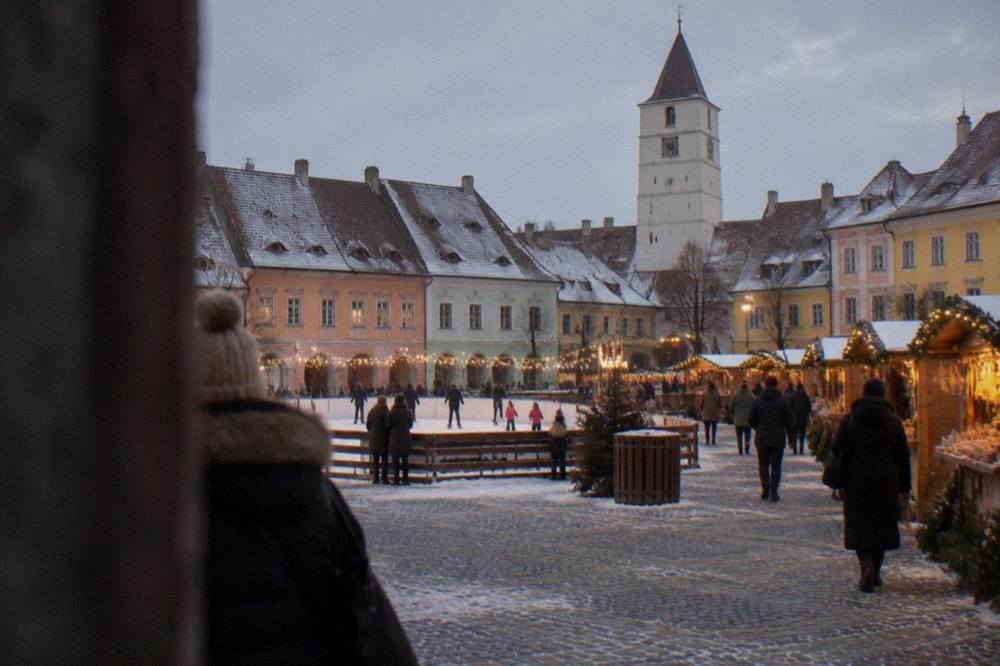 A Christmas market square at dusk with wooden stalls, string lights and an ice rink