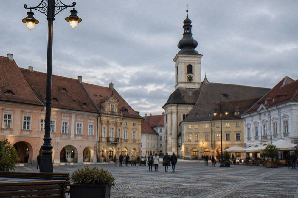 The grand square of Sibiu with historic facades and a church tower under an evening sky