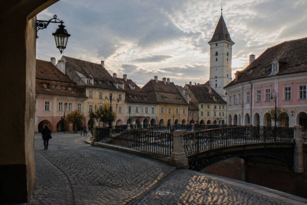 An old iron pedestrian bridge and pastel burgher houses in a small square at dusk