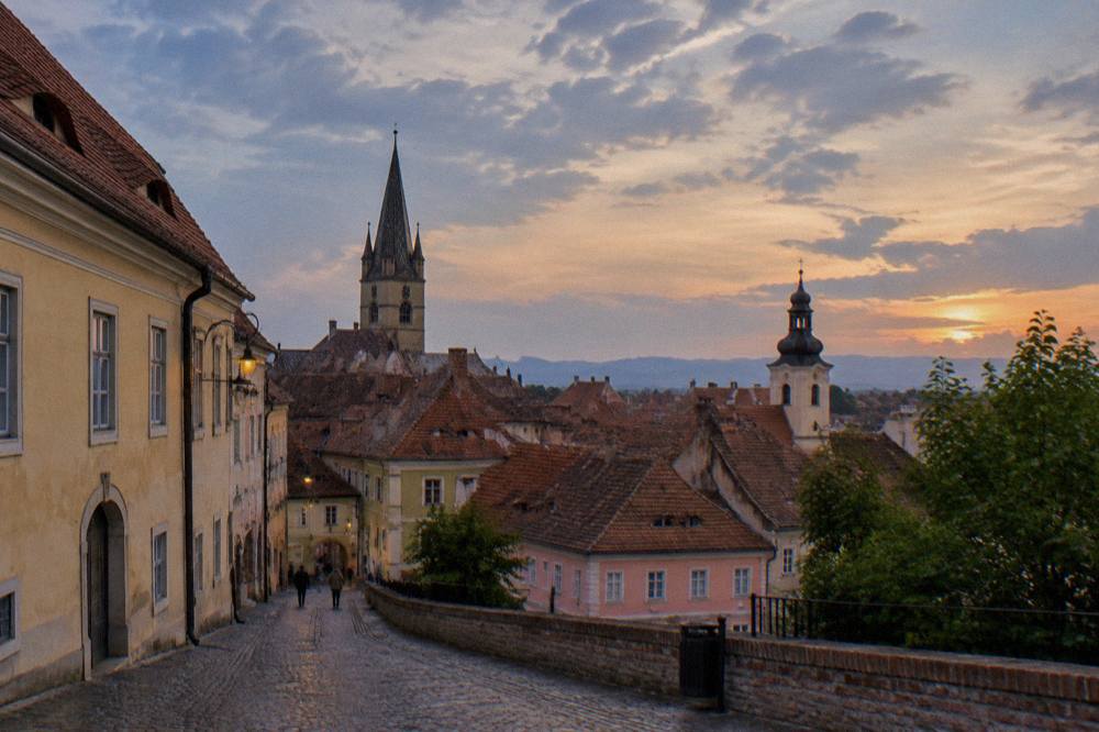 Cobblestone lane with the Sibiu old town skyline and church spires at dusk