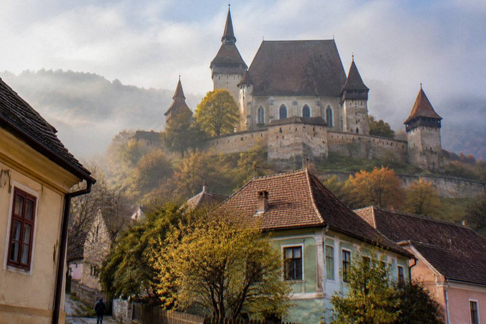 Autumn mist over a fortified church tower and village rooftops in Transylvania