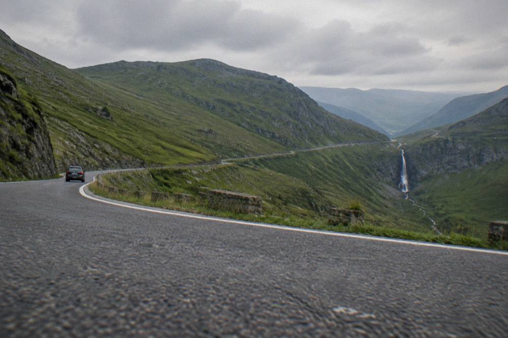 A wide mountain road curving along a green ridge high in the Făgăraș mountains
