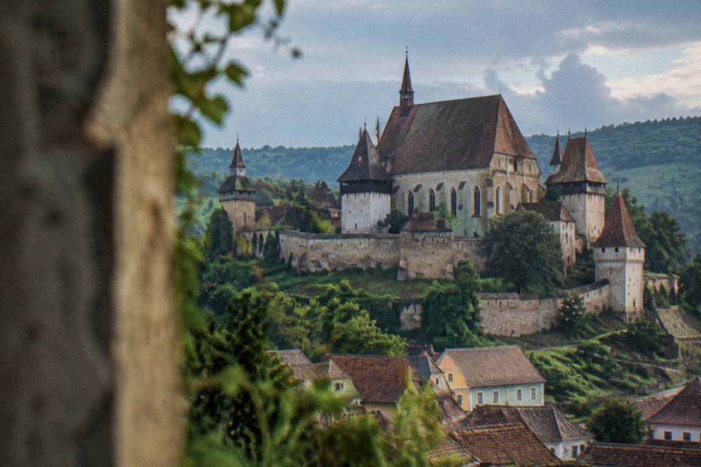 A fortified church with high walls and towers standing above a village in rural Transylvania