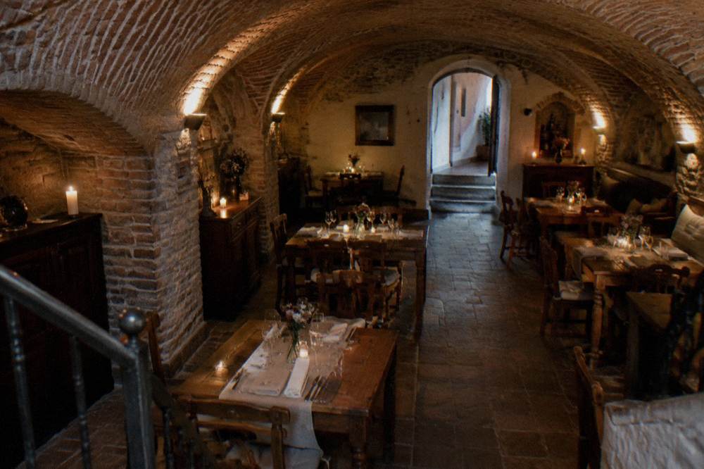 Vaulted brick cellar restaurant interior with wooden tables set for dinner