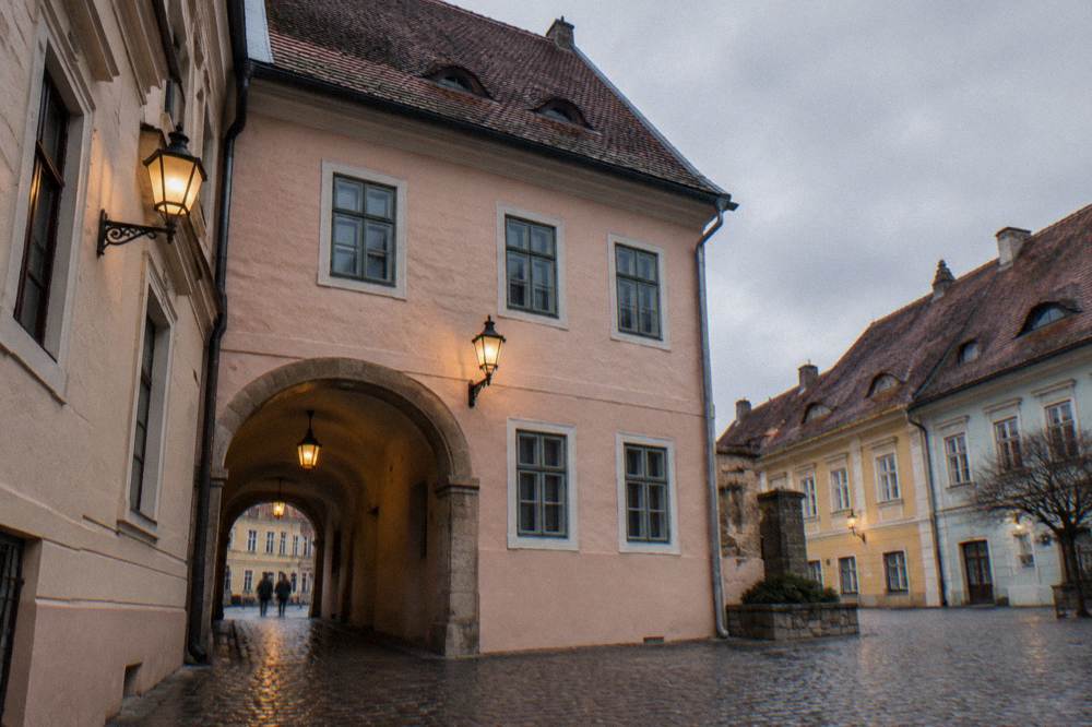 A covered stone passage on a wet grey day, lamps glowing against the damp walls