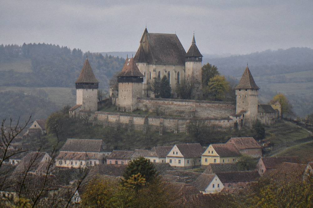 A fortified church with high defensive walls standing above a village in rolling countryside