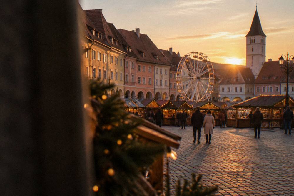 A festive market square at dusk with wooden stalls, lights and a ferris wheel