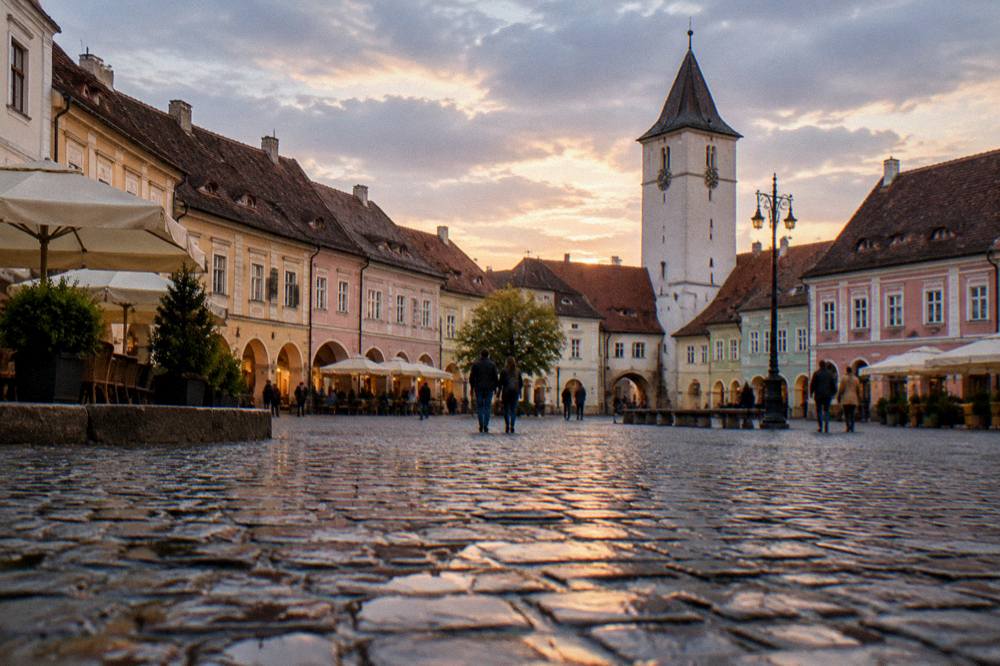 Evening light on a pedestrian square with medieval towers at its edge