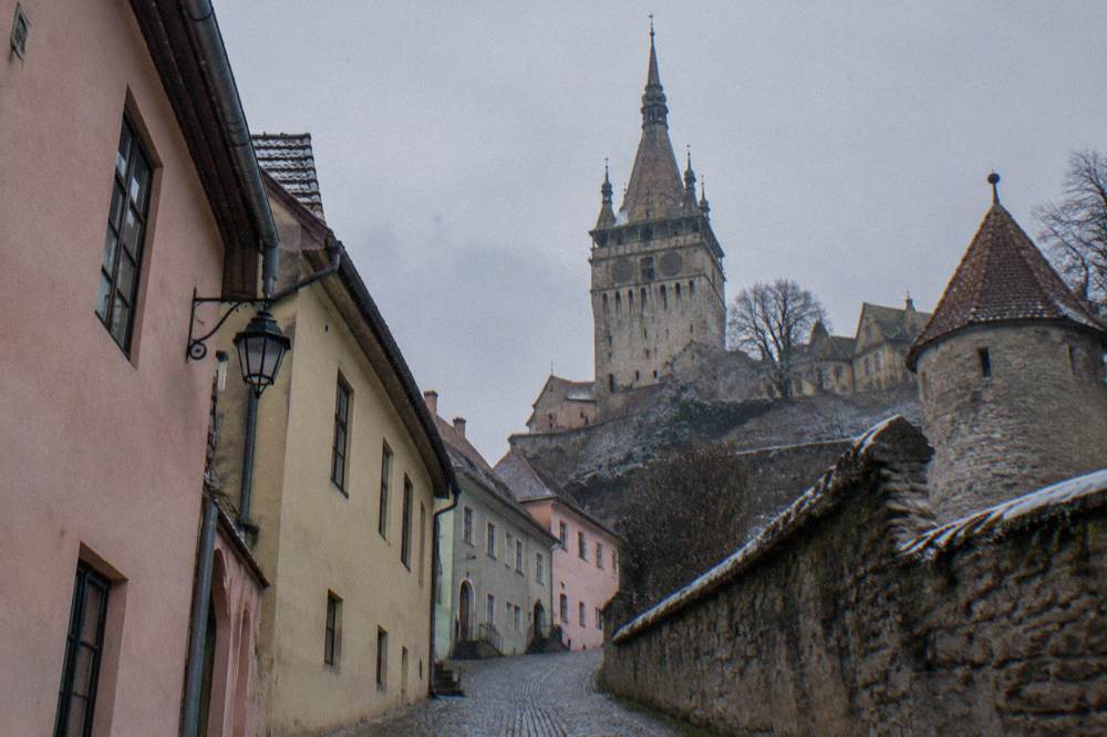 A pastel-coloured medieval clock tower above narrow cobbled streets in Sighișoara