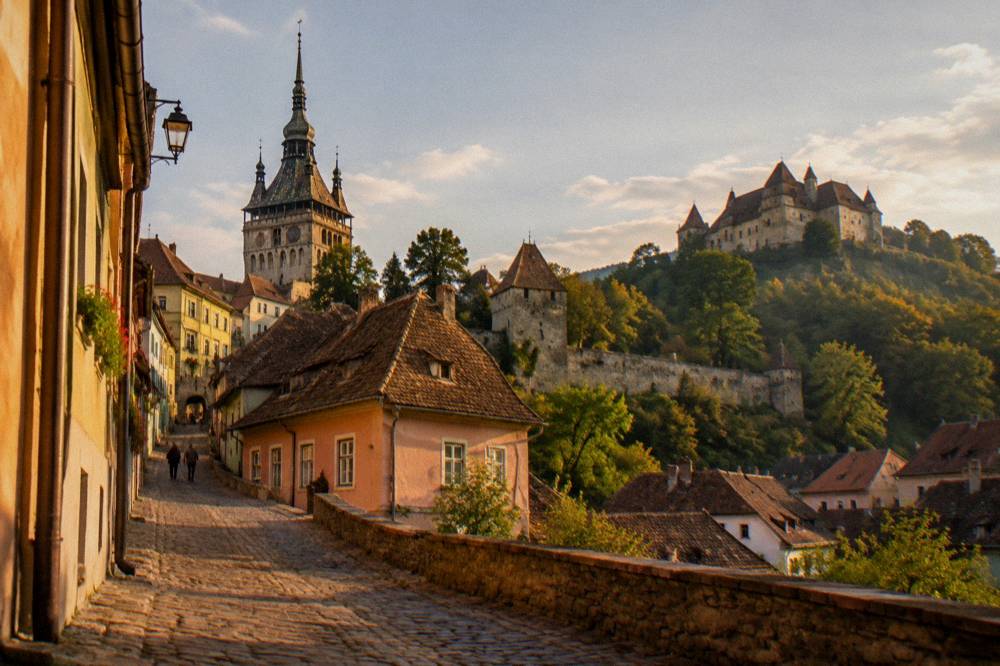A stone castle on a forested hillside above red rooftops in the Carpathian foothills