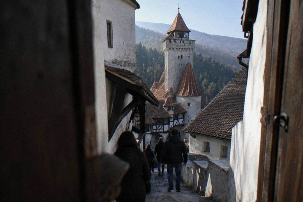 Visitors walking a narrow stone stairway inside Bran Castle between timber doors and white walls