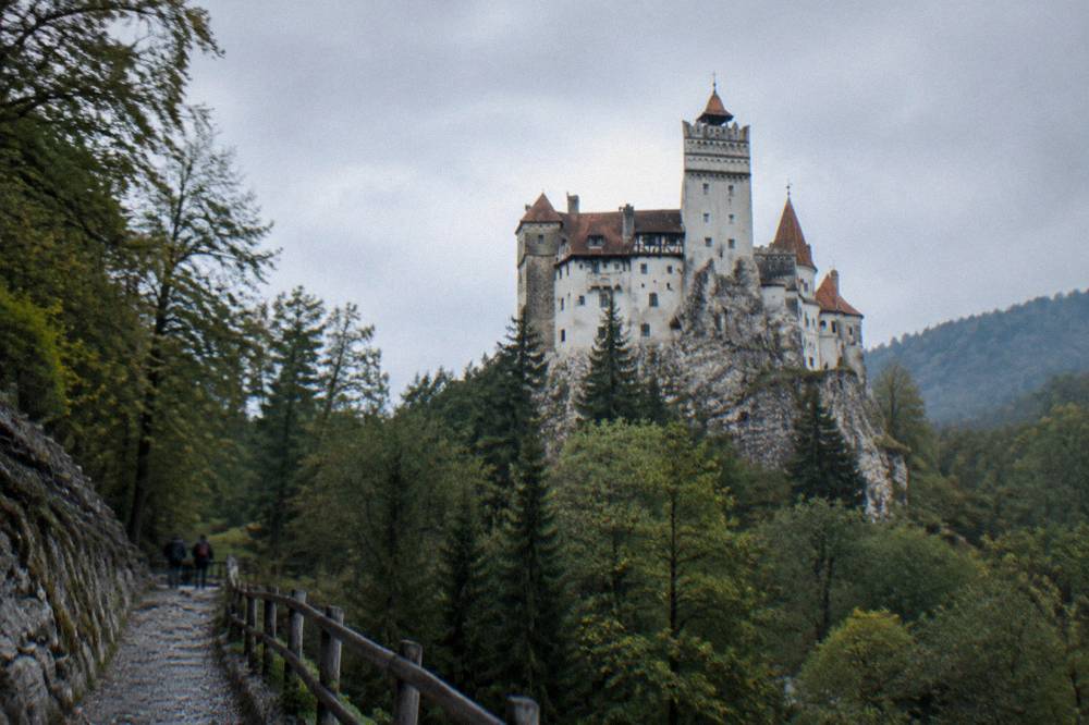 The red-tiled roofs and white towers of Bran Castle seen from the path below the cliff