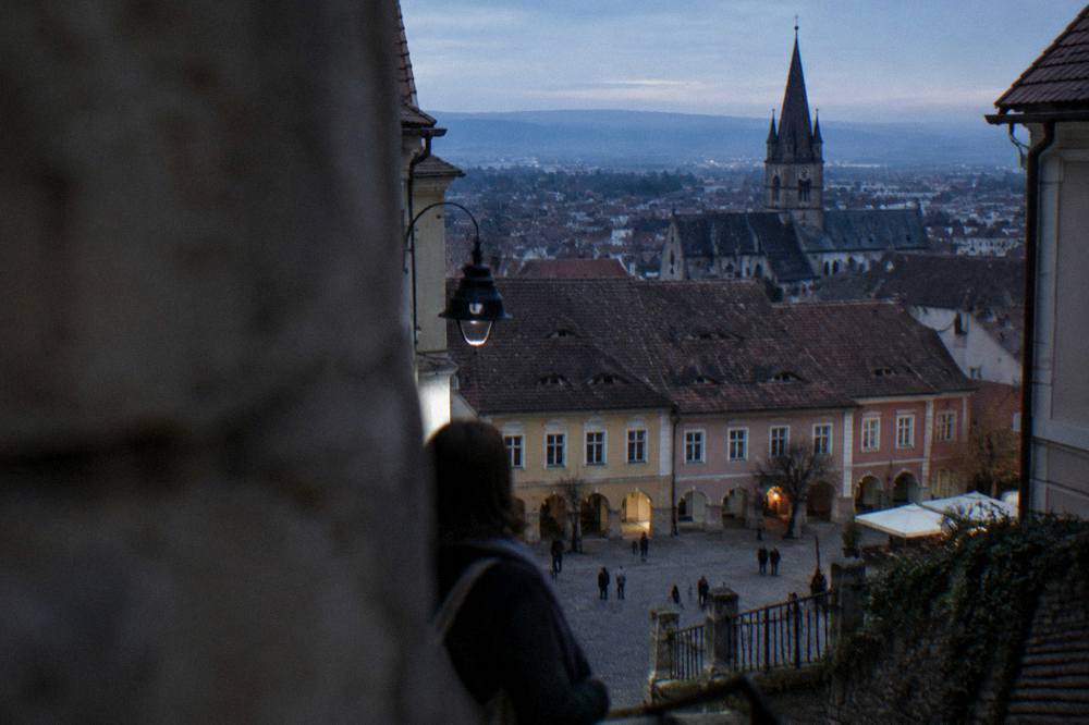 A tour minibus parked on a mountain road with Brașov's old town and dark church tower below
