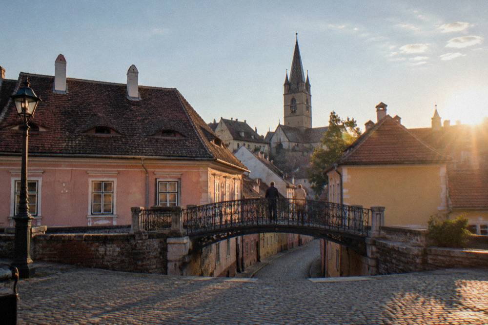The Bridge of Lies iron footbridge seen from a cobbled square in Sibiu at golden hour