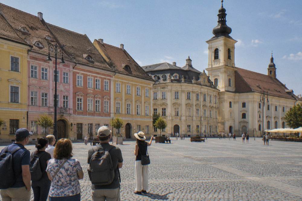 A tour guide gesturing toward the colourful facades of Sibiu's Great Square while a small group listens