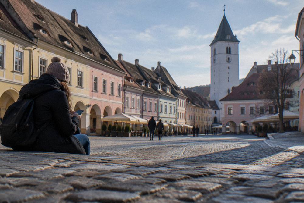 A visitor consulting a phone map beside the pastel-coloured burgher houses of Sibiu's Little Square