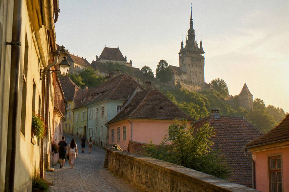 Travellers walking up a cobbled lane between pastel-coloured houses in Sighișoara